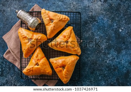 Homemade baked uchpuchmak (samsa) with meat and potato on a wire rack on a blue stone background. Top view and copy space.
