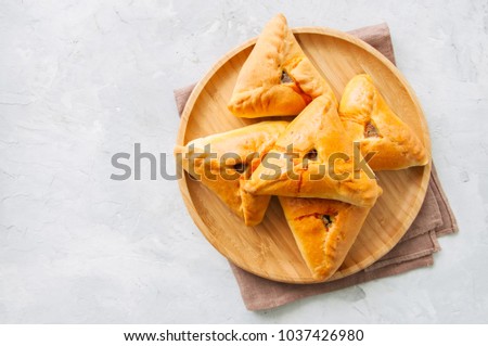 Homemade baked uchpuchmak (samsa) with meat and potato on a wooden plate on a white stone background. Top view and copy space.
