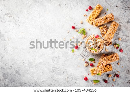 Healthy breakfast and snack concept, homemade granola with fresh raspberries in jar and nuts and granola bars, on grey stone stone background copy space top view