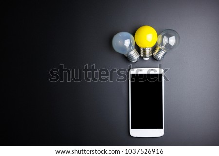 Smartphone and light bulb on black background with copy space