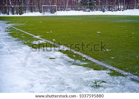 Football field in snow in the winter. A white marking on a green field and white gate for game in football.