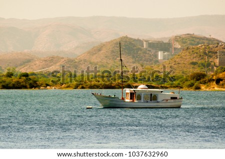 Ornate sail boat anchored on a blue lake with beautiful aravali hills in the background. Shot in Udaipur on the famed lake pichola in Rajasthan India