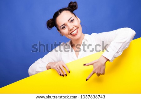 Happy smiling woman poiting to a yellow banner with copyspace availabe over blue background in studio photo
