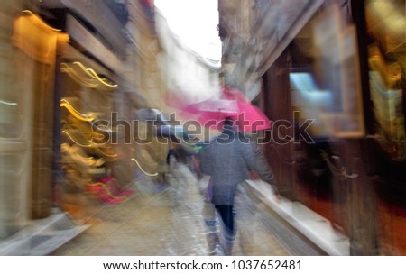 Impressionist photography at very low speed of people moving with umbrellas during a rainy day, inclined planes to give a sense of haste and sliding down a shiny, slippery and dangerous floor, 