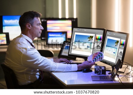 Side View Of A Mature Male Designer Holding Colorful Swatch Working On Computer In Office