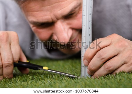 Close-up Of A Man Using Measuring Scale While Cutting Grass With Scissors Royalty-Free Stock Photo #1037670844