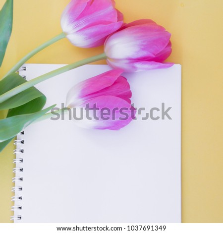 On a yellow background is a white notebook with pink tulips