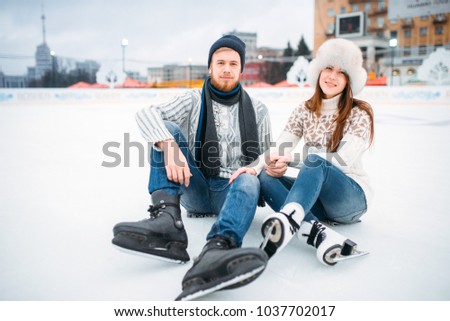 Love couple in skates sitting on ice, skating rink