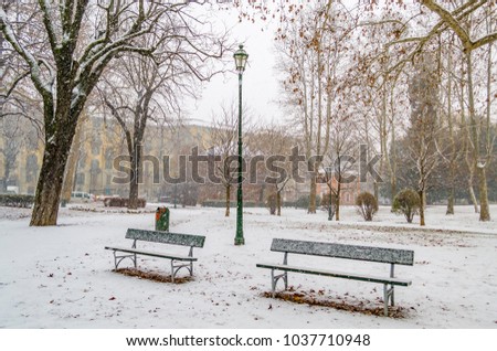 Panorama with benches covered with snow in the Giardini Reali public park in Turin (Piedmont, Italy) during a heavy snowfall in March.