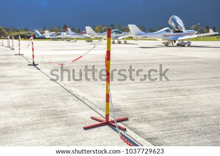 Red and yellow pole sign with a chain prohibits people of passing on an airport where small sport planes are parked and where they take off
