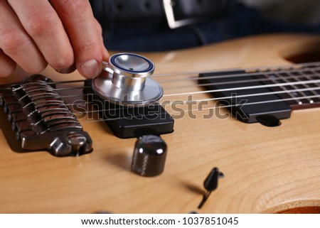 Male arms hold stethoscope head diagnosing guitar