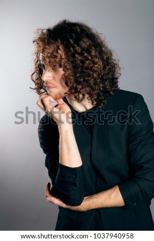 Attractive young man with long ginger curly hair in black blazer jacket and black t-shirt, smart casual outfit, studio portrait