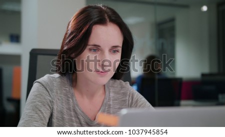 A young beautiful lady sitting in the office in front of a laptop. Closeup shot. Soft focus