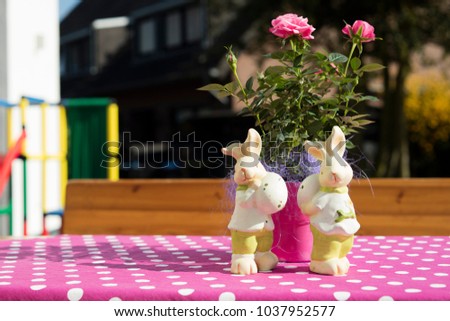 easter rabbits figurines on a pink table with a rose in a sunny day.