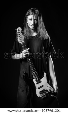 Dramatic studio portrait: a handsome long-haired young man (rock musician) holds electric guitar in hands. Black and white
