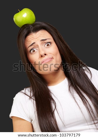 portrait of a young woman holding a green apple on her head over a black background