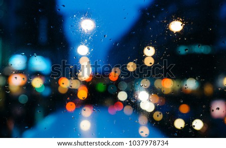 Emotional melancholic abstract background with defocused lights bokeh in London, UK behind rain drops in window glass, Focus on few drops due to the shallow depth of field