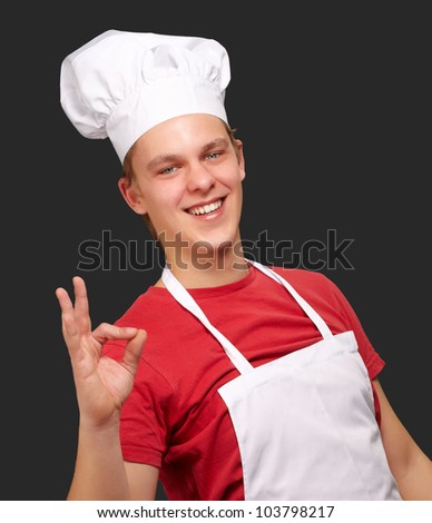 portrait of a young cook man doing a success symbol against a black background