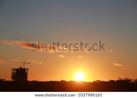 Skeleton of Building with Crane Scaffolding Under Construction at Sunset with Mostly Clear Sky a Few Scattered Orange Clouds