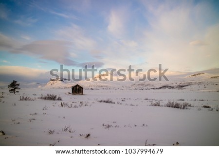 An old barn stands alone in front of majestic mountains in a beautiful winter wonderland