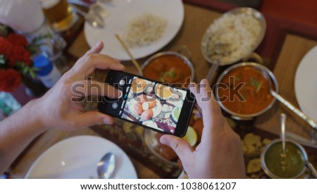 Close up of hands with smartphone taking a pic of indian food for social network site.