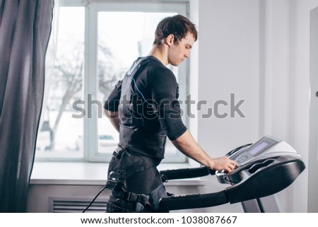 Fit Man in black electric muscle stimulation suit for ems training running on treadmill at gym