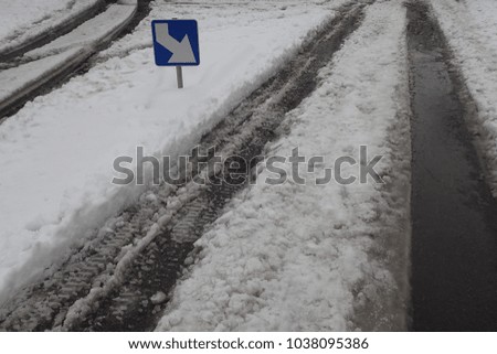 View of a blue and white traffic sign indicating the right hand direction. Dark traces cars on the snowy asphalt road. Abstract urban picture taken in France during the winter. Square element.  