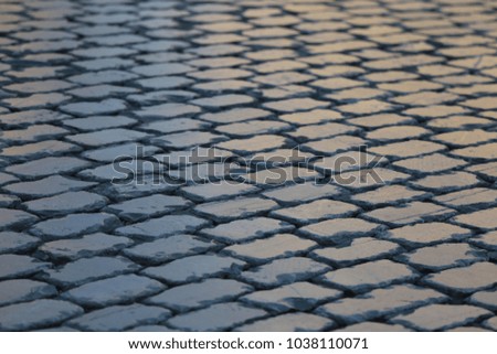 Close up outdoor view of the surface of a paved road. Pattern of grey granit cobblestones. Mosaic and geometric design. Abstract image with repetitive shapes and lines. Urban picture in the evening.