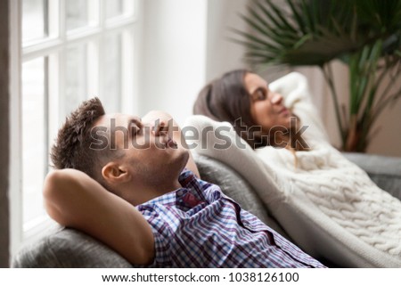 Young couple resting on comfortable couch together at home, happy man and woman enjoying relaxation or nap dozing on sofa with eyes closed, calm family breathing fresh air feeling totally relaxed Royalty-Free Stock Photo #1038126100