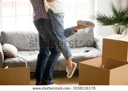 Happy couple on moving day concept, man lifting woman standing among cardboard boxes starting living together in new own house, husband holding embracing wife celebrating relocation, close up view Royalty-Free Stock Photo #1038126178