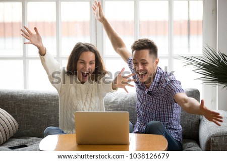 Young couple feeling excited by online win looking at laptop screen, happy man and woman celebrating victory watching video, screaming enjoying good news, motivated by achievement or great result Royalty-Free Stock Photo #1038126679