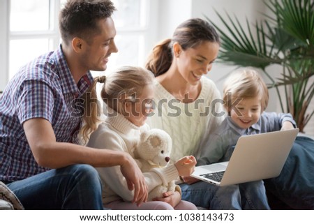 Young family with adopted children using laptop together at home, smiling parents and son daughter relaxing with computer looking at screen, married couple with kids shopping or watching video online