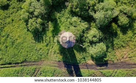 Rise above the water tower with rotation. HEAD OVER SHOT. View of the dirt road, meadow, bushes and potato field.  