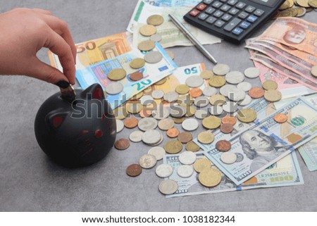 Euro, US Dollar, Hong Kong banknotes and multi currency coins from around the world a calculator a pen and a hand of a woman placing a coin in a cat piggy bank. The concet savings in a global economy.