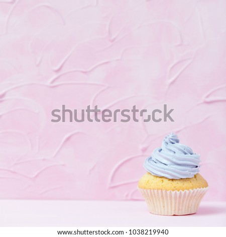 Cupcake decorated with violet buttercream on pastel pink background with copy space. Sweet beautiful cake for birthday greeting card or party invitation.
