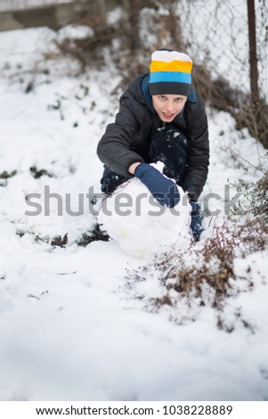 The boy is molded Snowman with a carrot in the yard in the winter, Teenager is playing with snow
