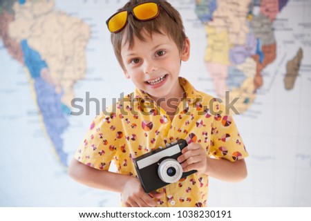 happy smiling boy in sunglasses and vintage camera in hands on background of world map