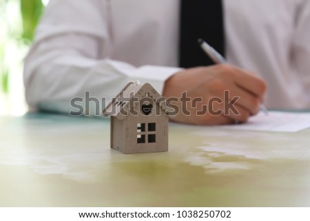 Real estate concept - businessman signs contract behind home model