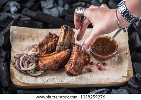 Grilled meat ribs, vegetables and sauce on a wooden board close-up. Fresh food on a dark background.