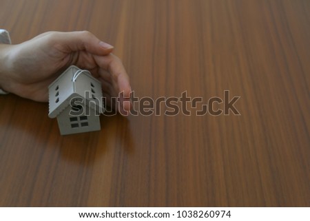 The building, mortgage, real estate and property concept - Businessman holding house on the wooden background