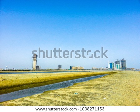 people are sitting on the benches in a  beautiful and bright day at a sandy beach and city building in the background and blue sky