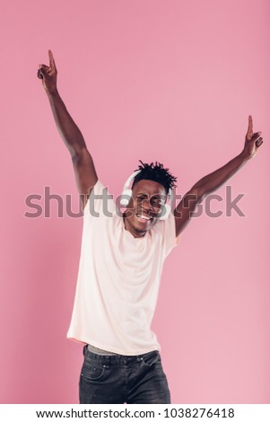 happy African-American man in headphones listening to music on pink background