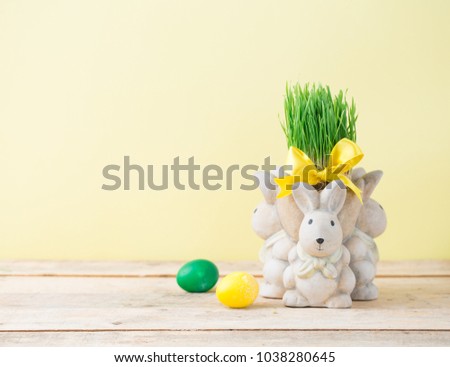Easter decoration with rabbit and green wheat grass, eggs in yellow and green colors, copy space, light green yellowbackground, pastel colors, satin ribbon tied bow wooden table white vase