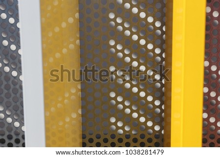 Close up outdoor view of a decorative colorful iron gate with a perforated grey sheet in background. Pattern with colored bands, shadows and white and gray aligned holes. Abstract architectural image.