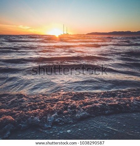 The raging sea, the waves close-up illuminated by the bright sun, the sailboat on the horizon
