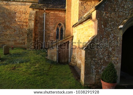 Image of a small stone church in the countryside with old mossy gravestones in the church yard during a brilliant sunset.  Church is in a small village (Evenload) in the Cotswolds, England.