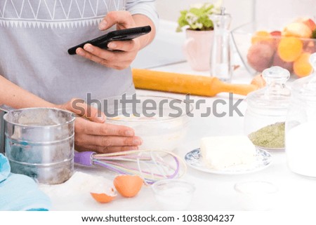 Closeup hands lady standing in kitchen and cooking the dough. Looking at tablet computer. Female following recipe on digital cooking healthy meal.