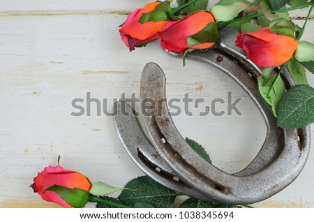 Two old horse shoes paired with silk red roses on a white-washed rustic wooden background makes a nice image with contrasting elements. Good for Kentucky Derby or any other equestrian theme. Royalty-Free Stock Photo #1038345694