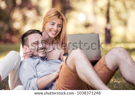 Young beautiful happy smiling couple sitting together in park on summer day,using laptop, laughing,having fun.