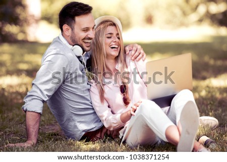 Young beautiful happy smiling couple sitting together in park on summer day,using laptop, laughing, having fun.